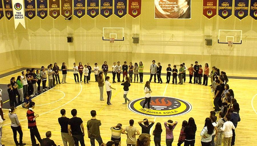 Gençlerin spor salonunda geniş bir çember halinde etkinlik yaptığı kamp